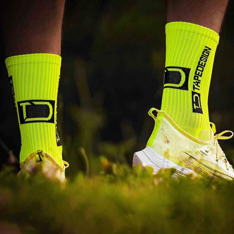 Žlté športové ponožky a bežecká obuv v tráve.