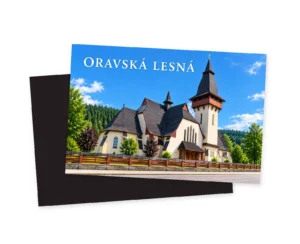 Náhľad magnetky s grafikou kostola svätej Anny v Oravskej Lesnej: svetlá veža, tmavé členité strechy, drevený plot a nápis ORAVSKÁ LESNÁ. Za prednou stranou je tmavý zadný diel.